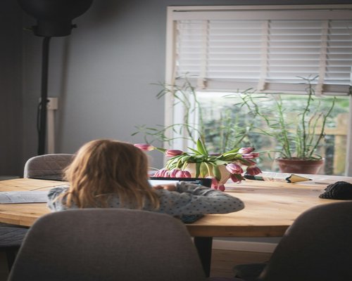A person working from home at a dining table setup, adjusting their sitting posture